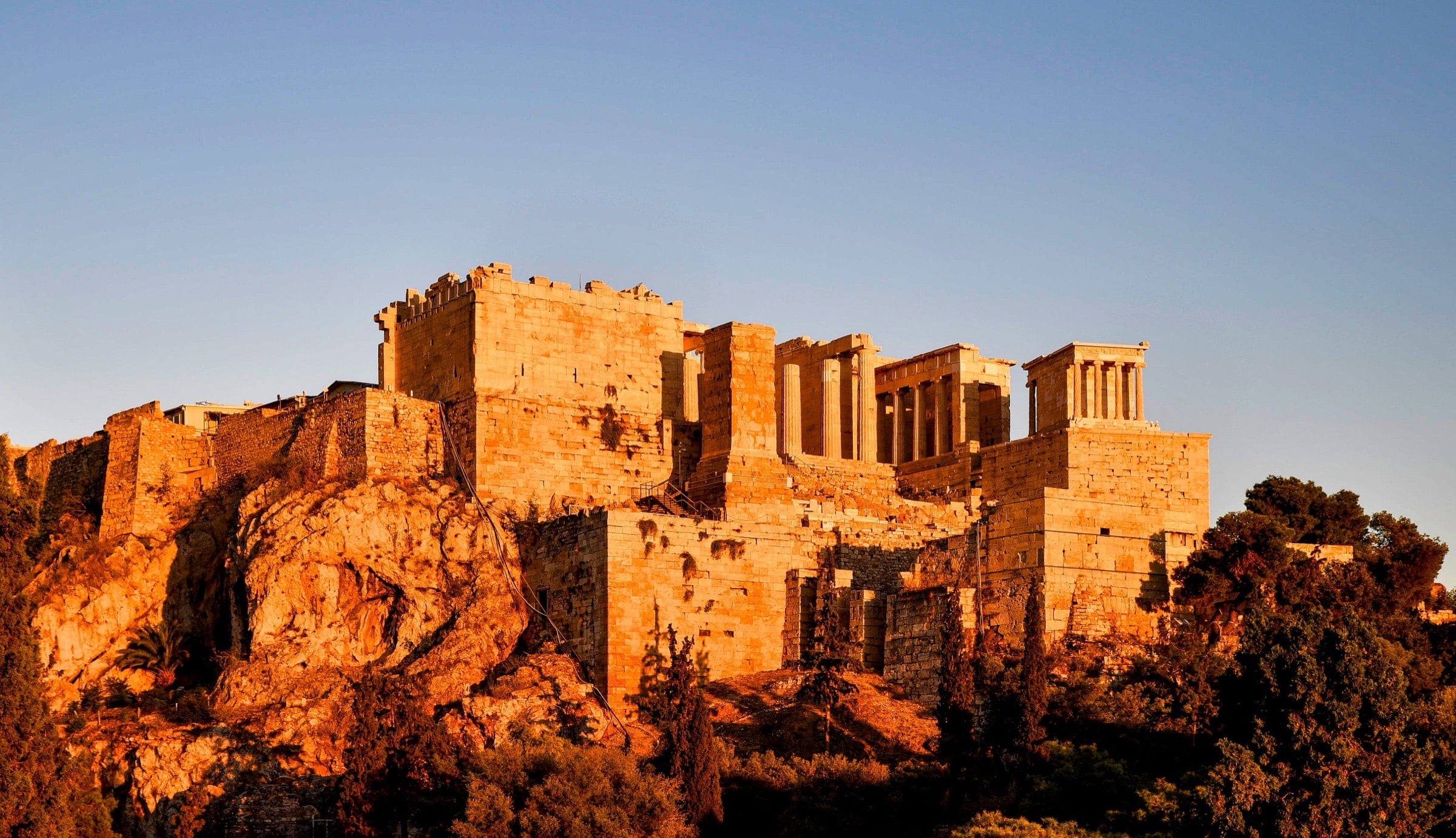 The Acropolis at golden hour — low evening sun turning the Propylaea deep amber above the rock