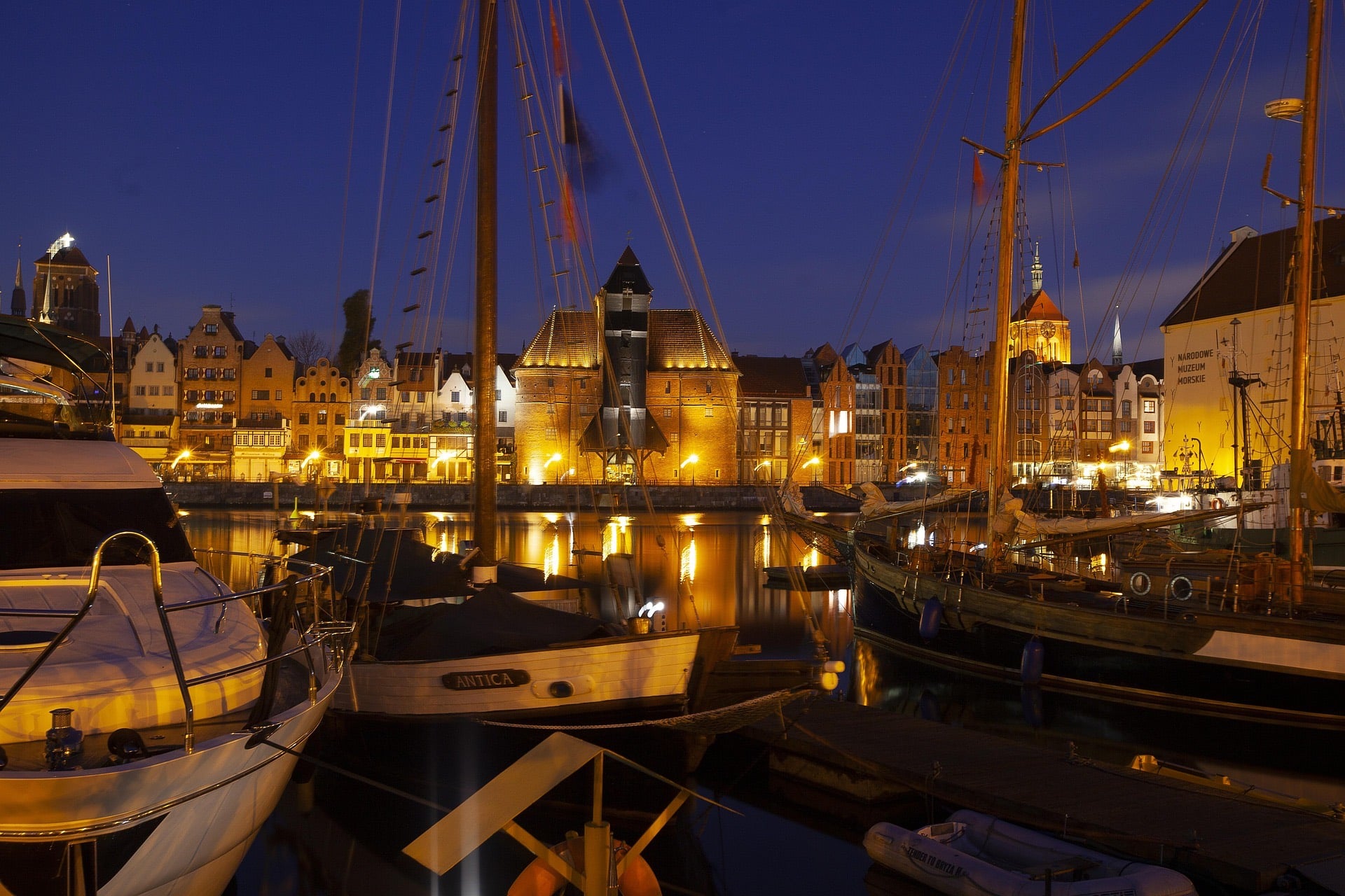 Sailboats moored on the Motława marina at night, the lit Żuraw crane beyond