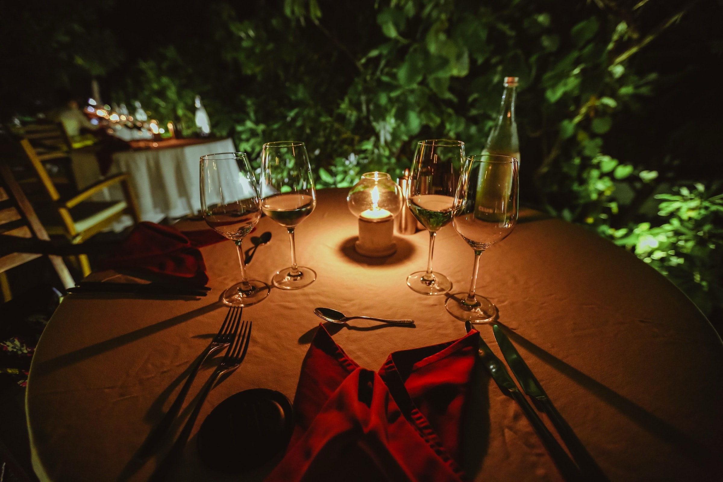 A candlelit dinner table laid with wine and greenery in warm evening light