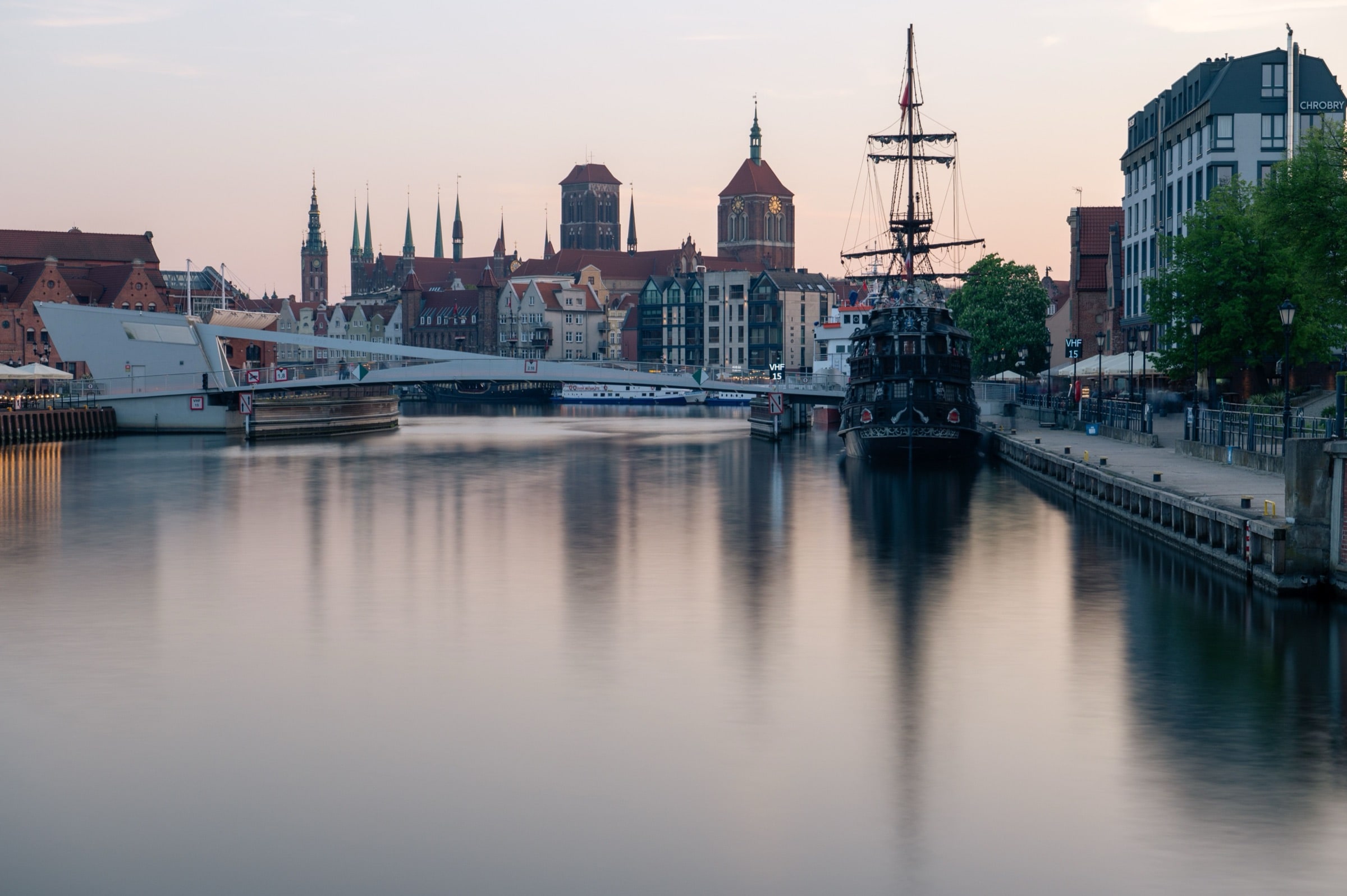 Sunset over the Motława in Gdańsk — the Old Town skyline and a moored galleon mirrored in the river